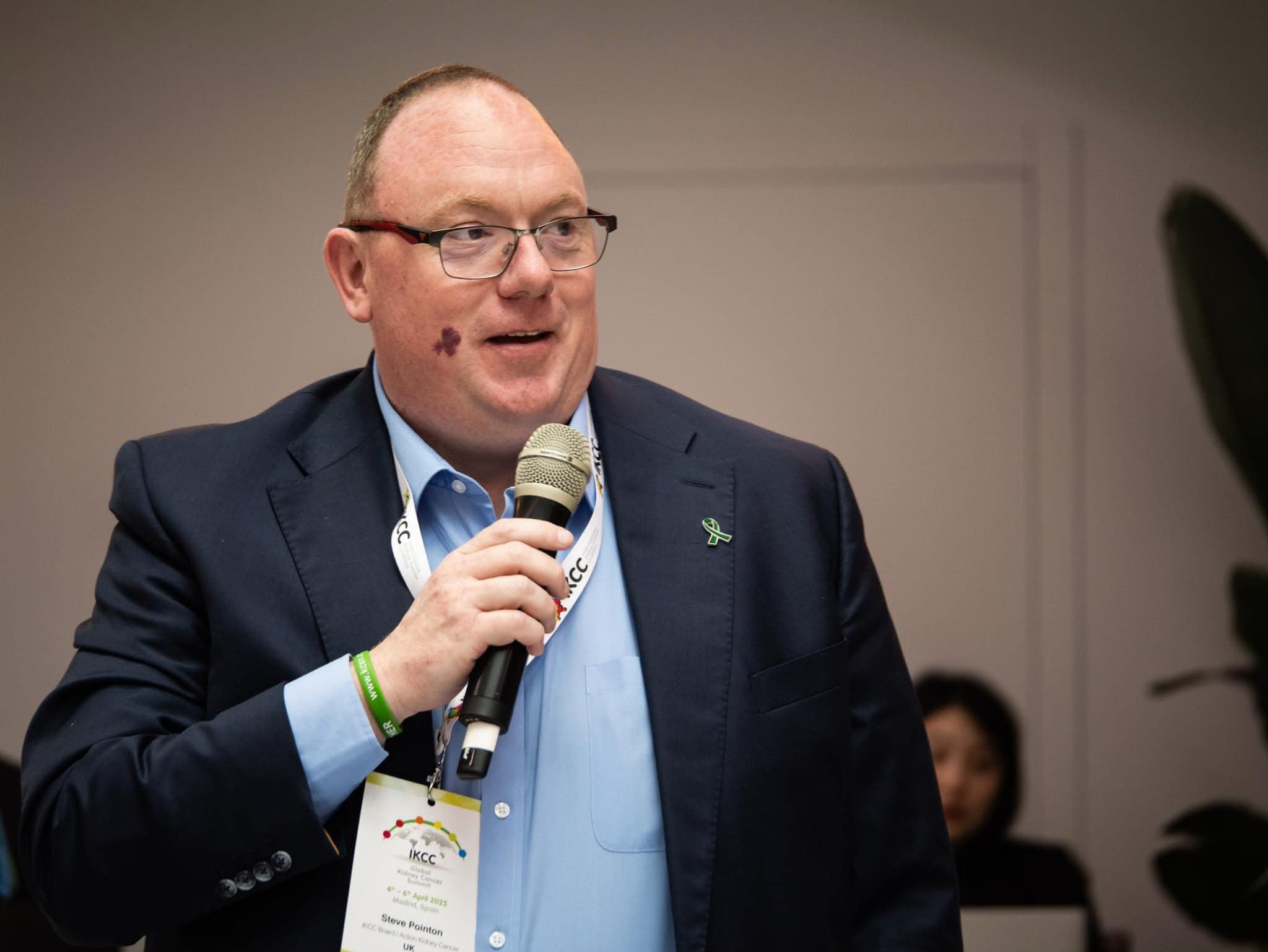 Steve Pointon speaking into a handheld microphone at the IKCC Global Kidney Cancer Summit in Madrid, 2025